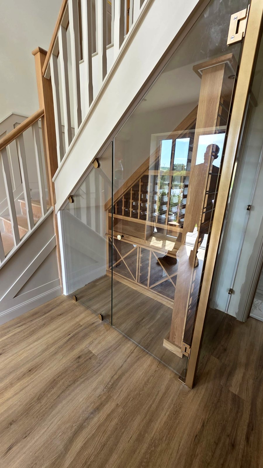 Under-stairs wine store glazed in toughened glass with brass fittings and an oak staircase, Warrington